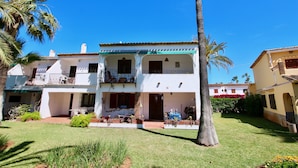 Una casa de dos pisos con balcón, un pequeño jardín y una palmera.