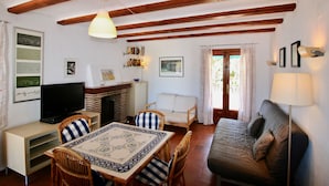 Una sala de estar acogedora con techo de madera, televisor, chimenea, mesa de comedor con sillas y sofá.