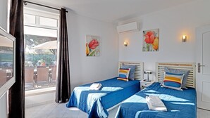Een hotelkamer met twee bedden, een raam met gordijnen, een wandairco en twee wandlampen.