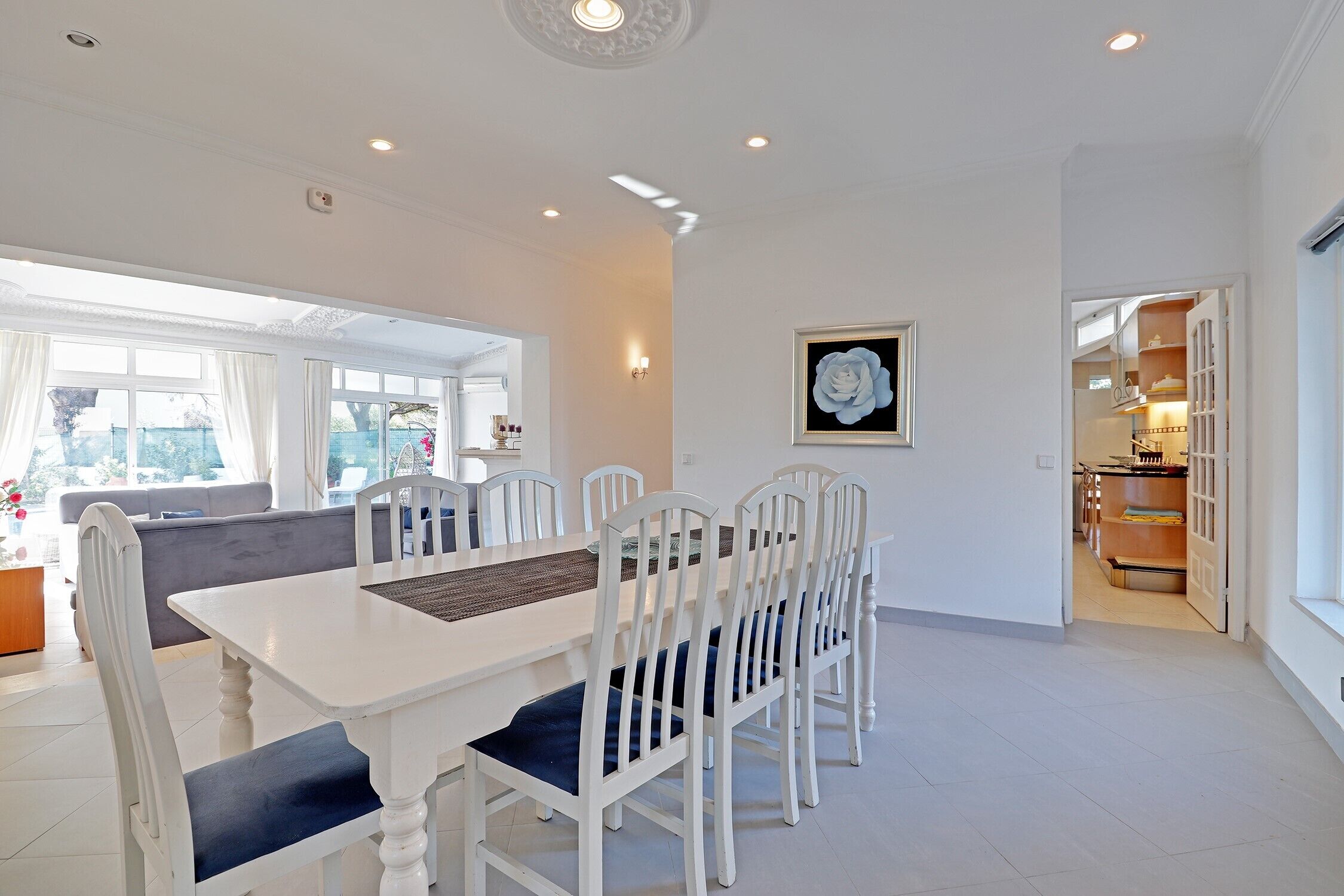 A dining area with a white table and chairs, a gray sofa, and a framed picture on the wall.