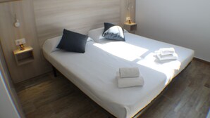 Un lit bien fait, avec des oreillers et une serviette pliée, une table de chevet avec une lampe et un plancher en bois.
