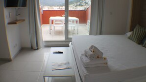 Une chambre d’hôtel avec un lit, un téléviseur fixé au mur, un balcon avec une table et des chaises, et une vue sur les montagnes.