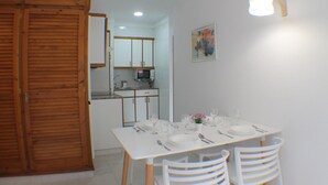 Un coin repas avec une table blanche dressée pour quatre personnes, des chaises en bois, un buffet blanc et un four à micro-ondes en arrière-plan.