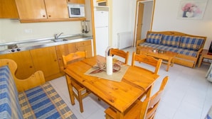 A compact kitchen with wooden cabinets, a microwave, and a sink. There is a dining table with chairs and a sofa with plaid cushions. - Rescator Resort 215 - One Bedroom Apartment, Sleeps 4 (Roses)
