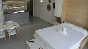 A hotel room with a bed, a small desk with a chair, a kitchenette, and a bathroom.