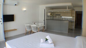 A hotel room with a bed, a small dining table with chairs, a kitchenette, and a TV mounted on the wall.