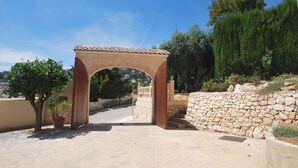 An arched stone gateway leading to a stone pathway, surrounded by potted plants and a stone wall. - Villa Luna del mar Su (Benissa)