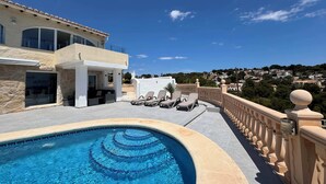 A pool area with a clear blue pool, lounge chairs, and a view of a hillside town. - Villa Luna del mar Su (Benissa)