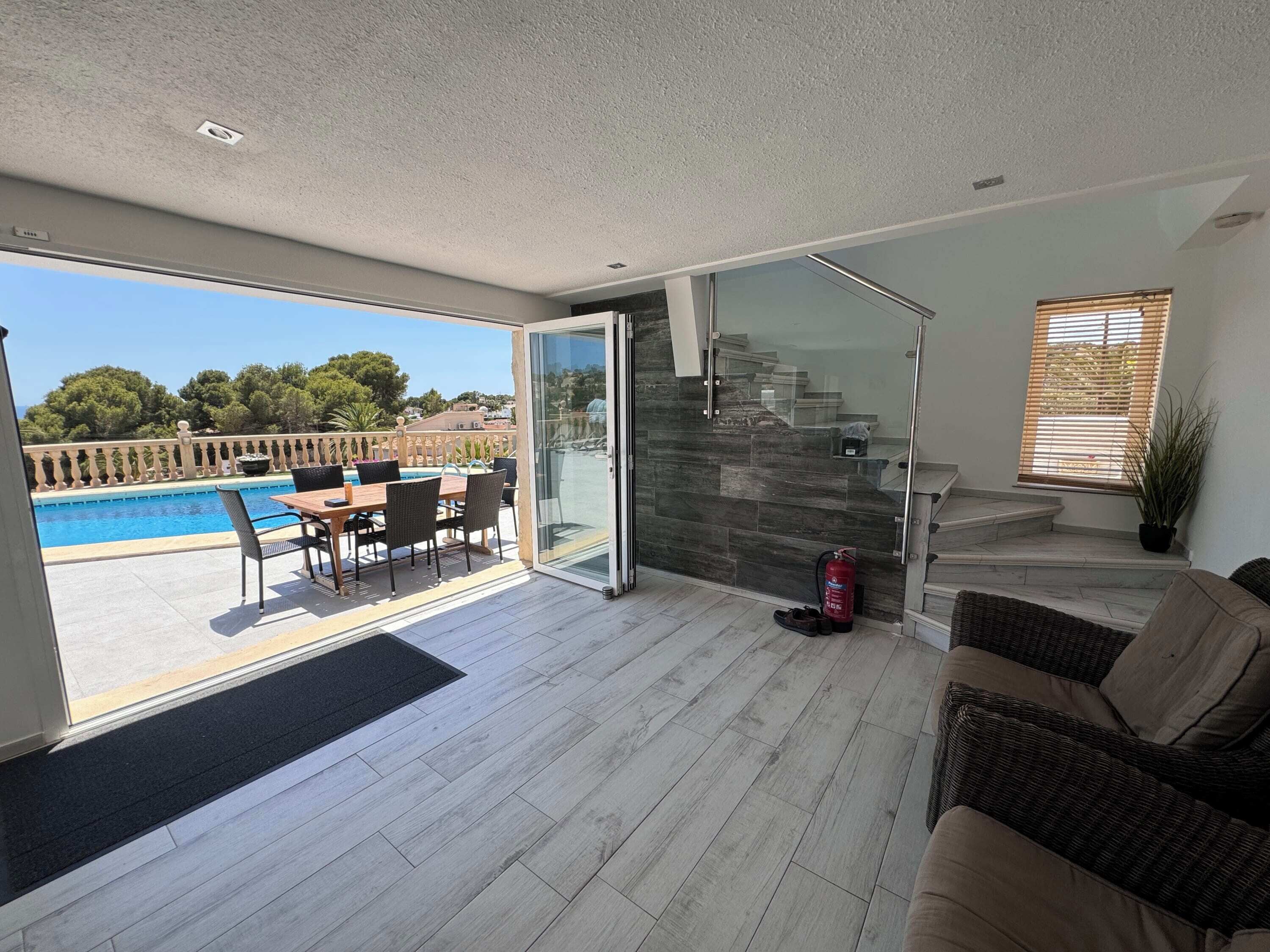 Un salon moderne doté d’une porte vitrée donnant sur une zone piscine, d’un escalier et offrant une vue sur l’extérieur.