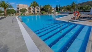 Ein Swimmingpool mit klarem, blauem Wasser, umgeben von Palmen und einem modernen Gebäude im Hintergrund.