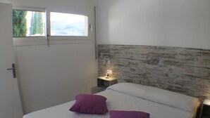 A bedroom with a bed, two purple pillows, a nightstand with a lamp, and a window with a view of mountains. - Rescator Resort 302 - Two Bedroom Apartment, Sleeps 6 (Roses)