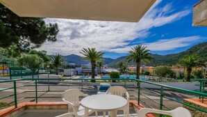 Une terrasse extérieure avec des chaises et une table en plastique blanc, offrant une vue sur une piscine et un paysage montagneux.