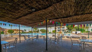 Un espacio al aire libre con mesas y sillas, una piscina al fondo y banderas coloridas.