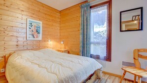 A wooden-paneled room with a bed, a chair, a window with curtains, and a framed mirror on the wall. - Fanyon 9 : Central one bedroom + sleeping area (MORZINE)