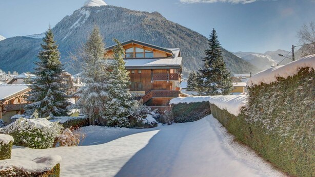 A wooden lodge with a balcony, surrounded by snow-covered trees and mountains in the background. - Fanyon 9 : Central one bedroom + sleeping area (MORZINE)