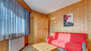 A wooden-paneled room with a red sofa, a wooden table, a radiator, and a painting on the wall. - Fanyon 9 : Central one bedroom + sleeping area (MORZINE)