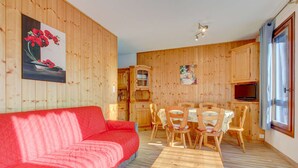 A cozy room with a red sofa, wooden dining table, and chairs. There is a wooden cabinet and a television in the corner. - Fanyon 9 : Central one bedroom + sleeping area (MORZINE)