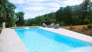 A rectangular swimming pool with clear blue water, surrounded by a light-colored tiled deck. There are three grey lounge chairs aligned along the pool's edge. - Villa for 6 People with Pool and Unobstructed View (LA LONDE LES MAURES)