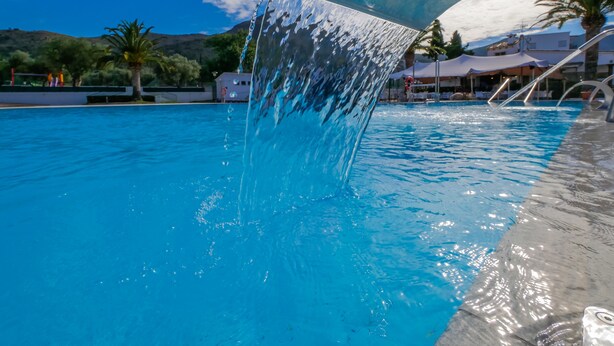 A swimming pool with clear blue water, a water feature, and a view of the surrounding area including palm trees and buildings. - Rescator Resort 225 - One Bedroom Apartment, Sleeps 4 (Roses)