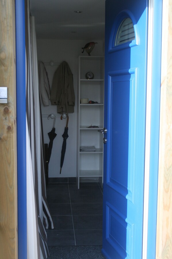 A blue door leading to a room with a white shelf, a clock, and two umbrellas.