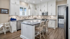 Una cocina amplia con muebles blancos, una isla central e iluminación colgante.