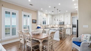 Una cocina amplia con muebles blancos, una isla central y un comedor con mesa y sillas de madera.