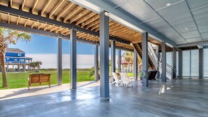 Un amplio espacio techado al aire libre con suelo de hormigón, vigas de madera y grandes ventanales.