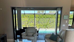 A spacious living room with a large window, a pool, and a 'Beach House' sign.