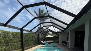 A covered swimming pool with a glass ceiling, surrounded by a patio area with chairs and a table.