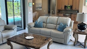 A spacious living room with a large sofa, a coffee table, and a view of a swimming pool through glass doors.