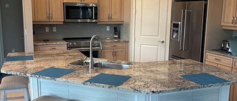 A kitchen with wooden cabinets, a stainless steel refrigerator, a microwave, and a granite countertop.