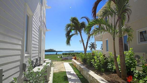 A well-maintained garden with a pathway leading to a beach view, palm trees, and a clear sky. - Anchor Point Apartments (Governor's Harbour)