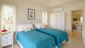 A bedroom with two beds, white walls, a framed picture, and a bathroom visible through an open door. - Anchor Point Apartments (Governor's Harbour)
