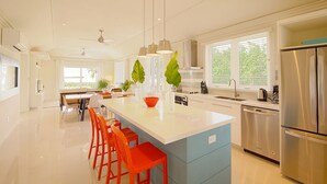 A modern kitchen with a central island, stainless steel appliances, and bright orange chairs. - Anchor Point Apartments (Governor's Harbour)