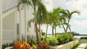 A white house with a stone planter bed, palm trees, and a pathway leading to the water. - Anchor Point Apartments (Governor's Harbour)