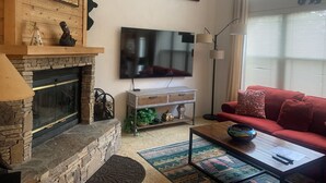 A cozy living room with a stone fireplace, a flat-screen TV mounted on the wall, a red sofa, and a coffee table with a bowl. - Experience All 7 Springs Has to Offer in This Great Townhouse (Champion)