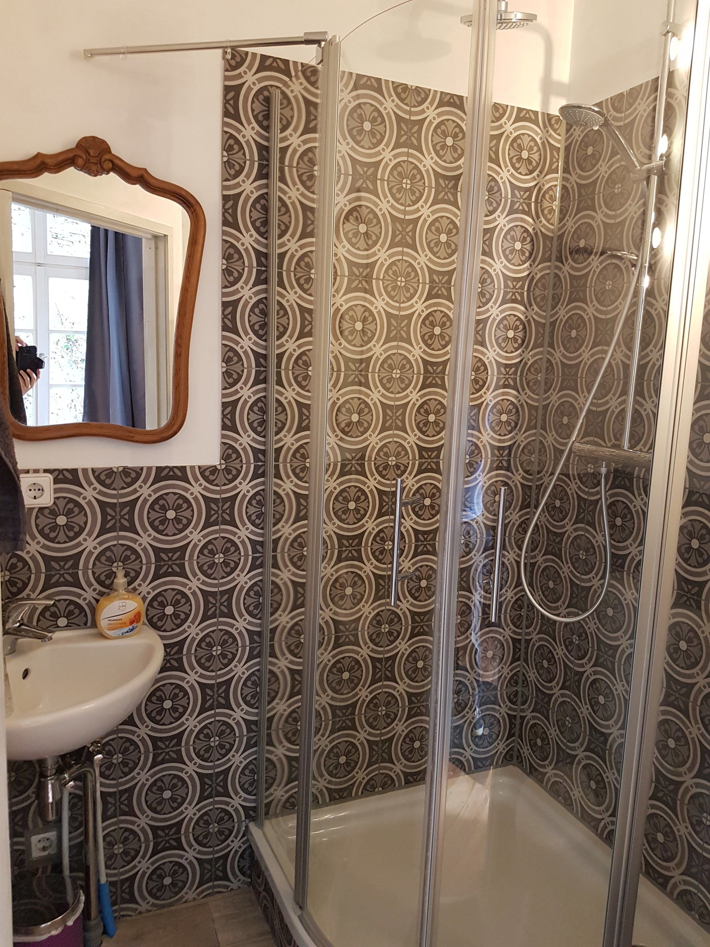 A bathroom with a glass shower enclosure, a sink with a soap dispenser, and a mirror with a wooden frame.