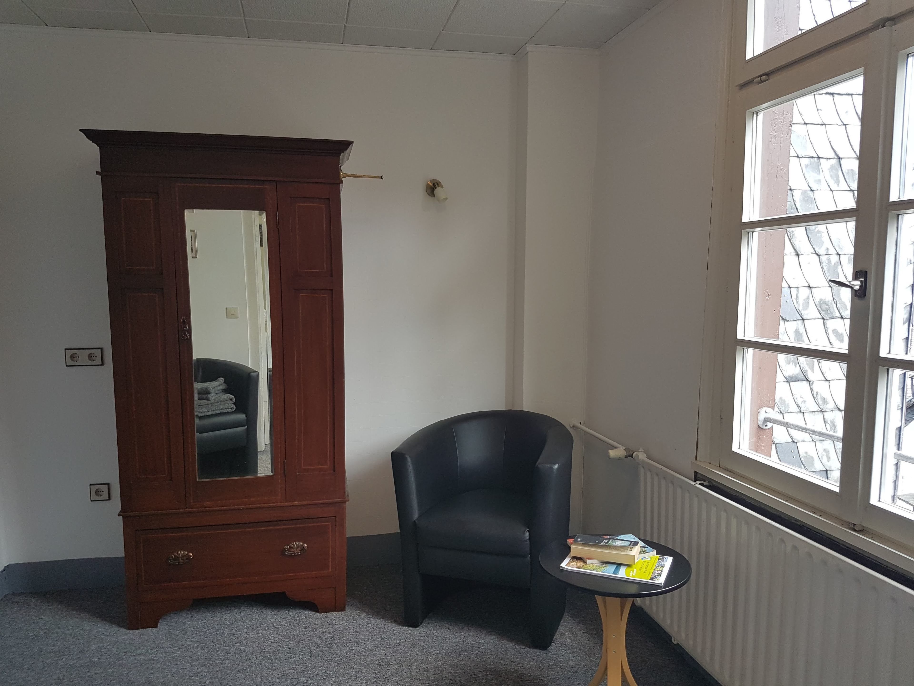Een kamer met een houten garderobe, een zwarte stoel en een klein tafeltje met boeken.
