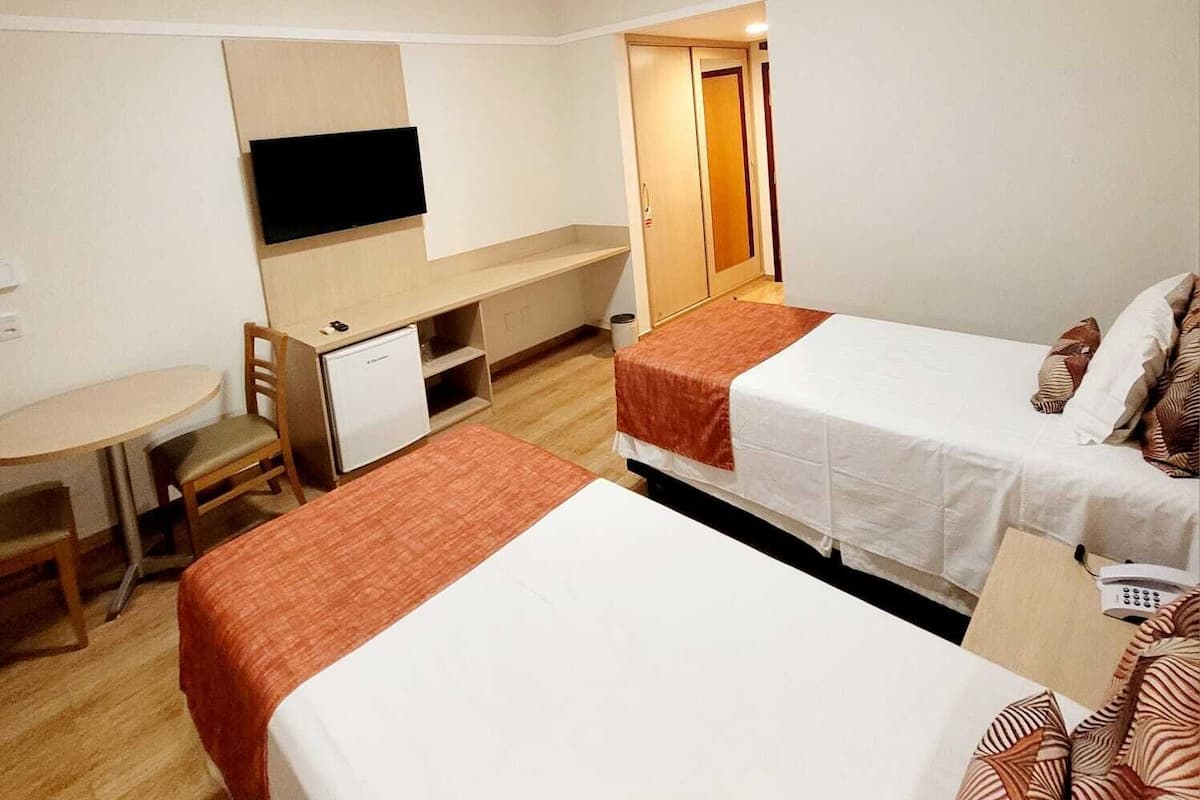 Une chambre d’hôtel avec deux lits, un bureau, une télévision et une armoire.