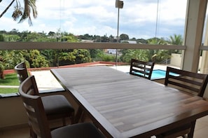 A wooden dining table with four chairs, a view of a swimming pool, and lush greenery in the background. - Hotel Giordano Mantiqueira (Sao Joao da Boa Vista)