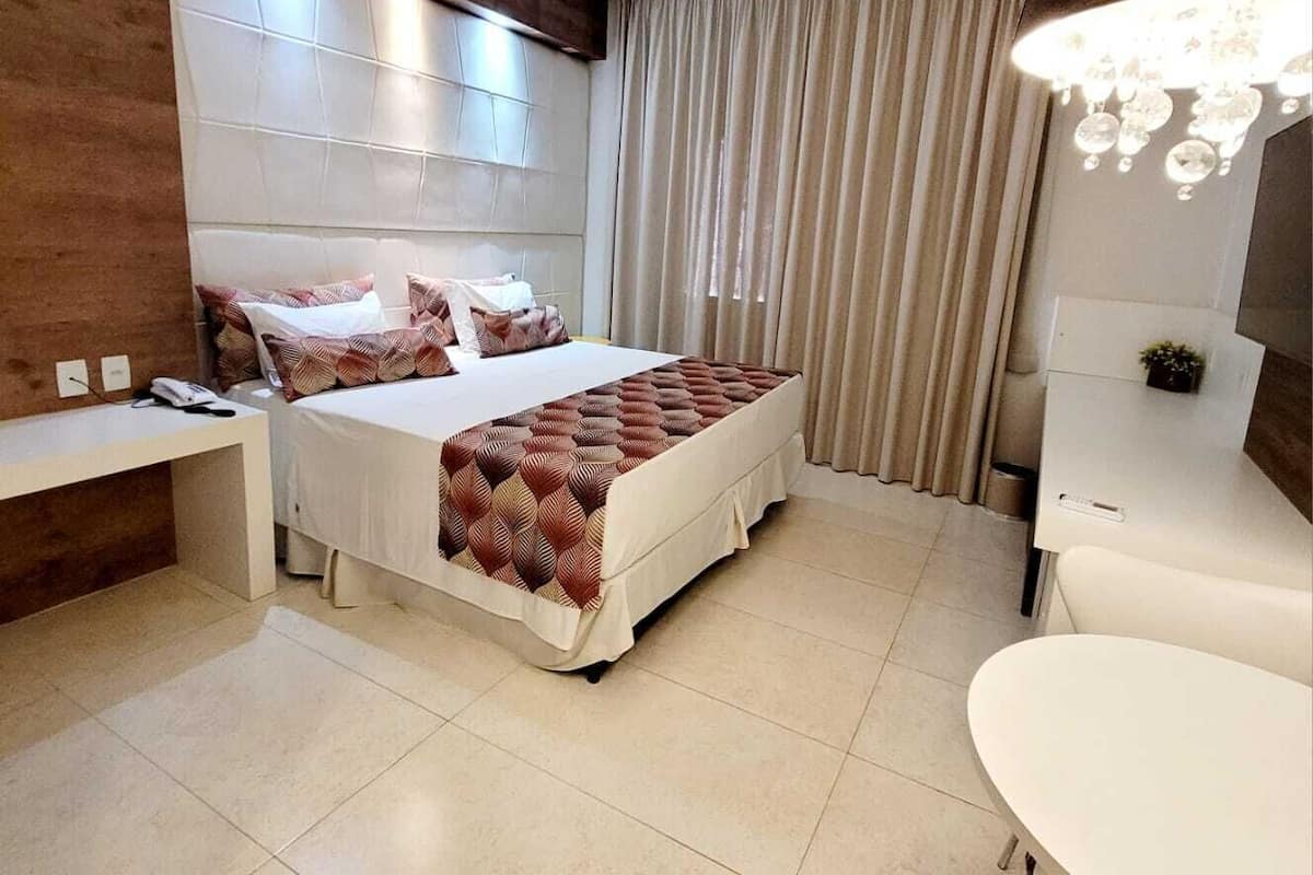 Une chambre d’hôtel moderne, dotée d’un grand lit, d’une table de chevet, d’un bureau, d’une chaise et d’une coiffeuse avec un miroir.
