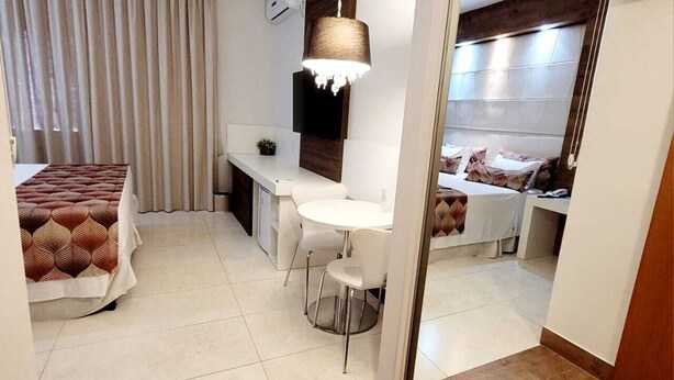 A modern hotel room with a bed, a desk, and a seating area. There is a large mirror on one wall, and the room has a tiled floor. - Hotel Giordano Mantiqueira (Sao Joao da Boa Vista)