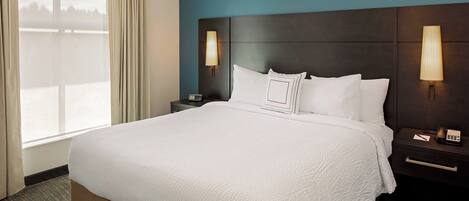 Una habitación de hotel con una cama grande, dos mesitas de noche, una lámpara y un ventanal con cortinas.