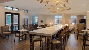 A spacious hotel lobby with a long central bar, multiple seating areas, and large windows offering views of the outside. - Residence Inn by Marriott  Charleston Summerville (Summerville)