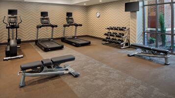 A gym with treadmills, elliptical machines, dumbbells, and a bench.
