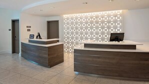 Un espace d’accueil comprenant deux comptoirs de réception en bois, un mur décoré d’un motif et un sol carrelé.