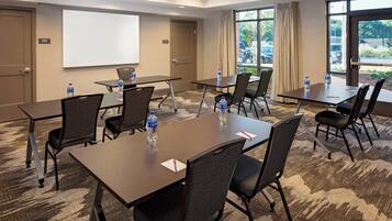 A conference room with multiple tables and chairs, a whiteboard, and a large window with a view of the outdoors.