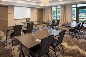 Un salón de conferencias con varias mesas y sillas, una pizarra y un amplio ventanal con vistas al exterior.