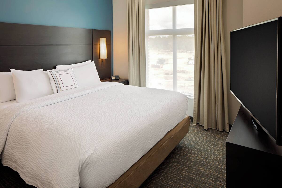 Una habitación de hotel con una cama grande, un televisor, una mesita de noche y una ventana con cortinas.