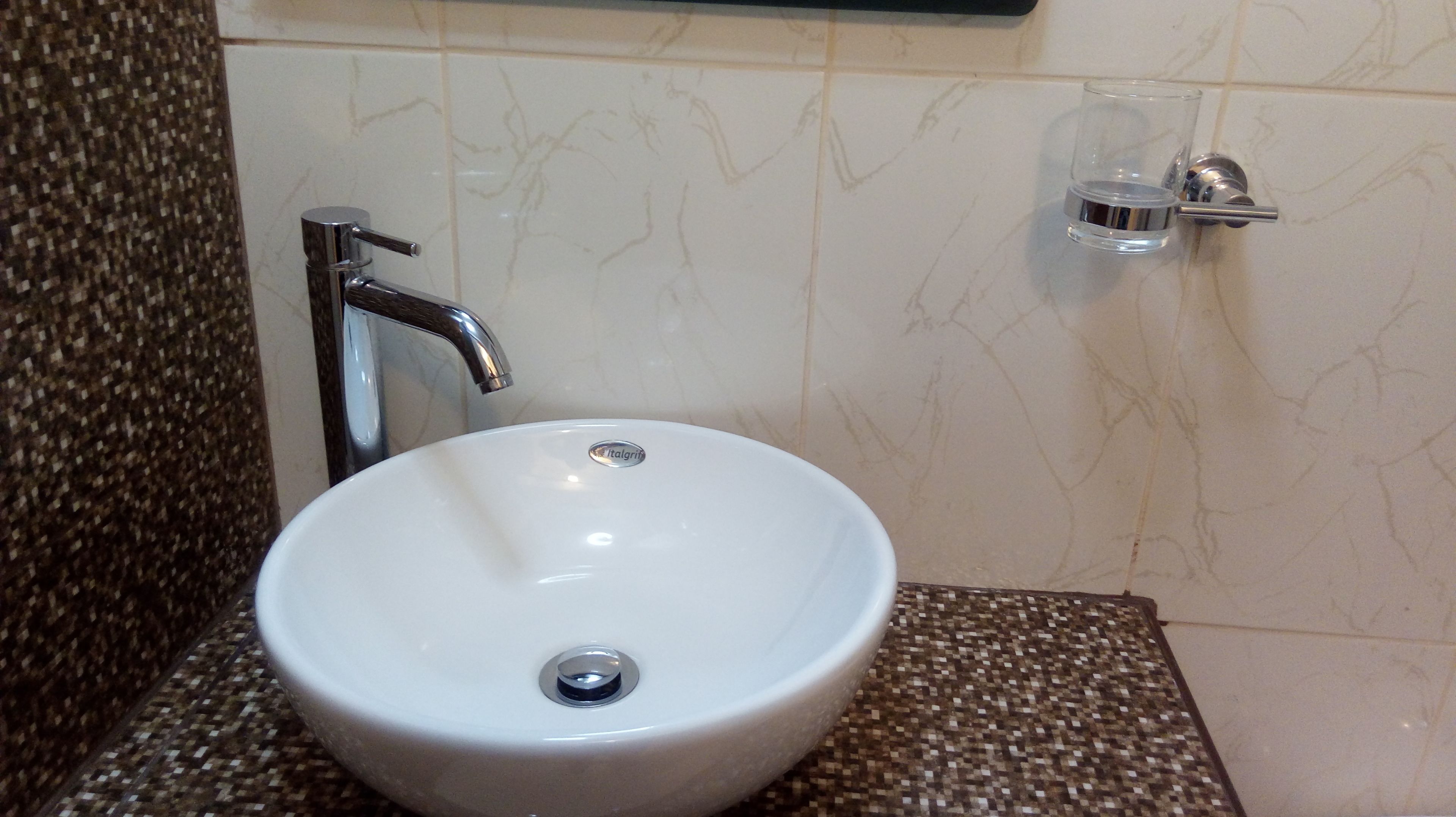 A bathroom with a white sink, chrome faucet, and a small glass container on the wall.